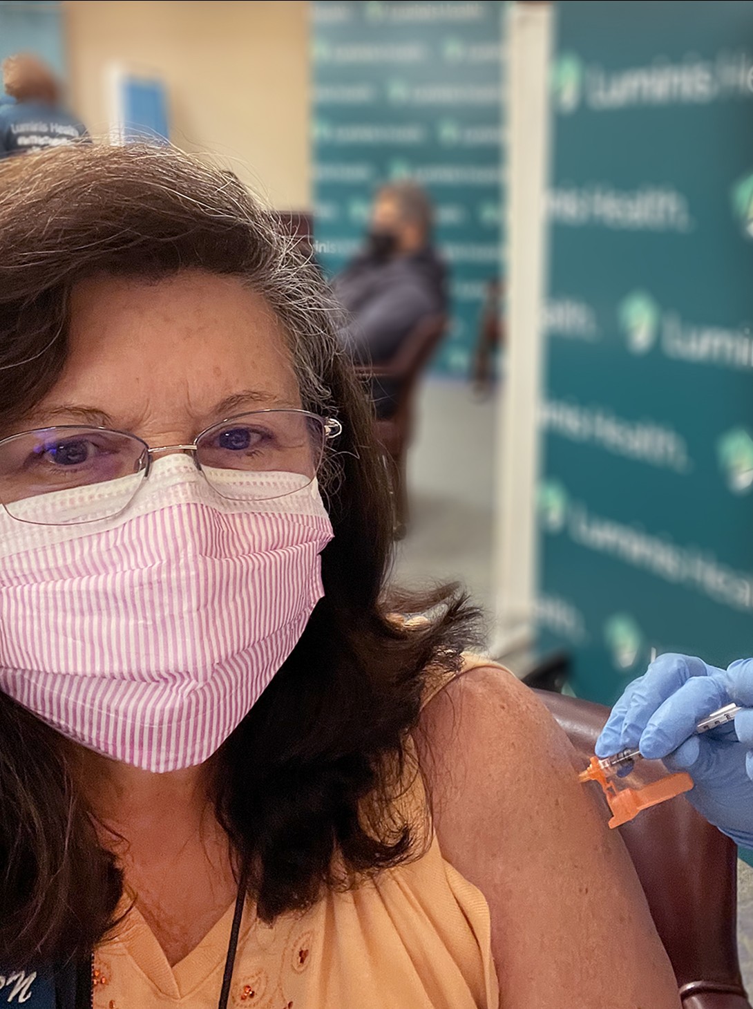 Woman with brown hair wearing glasses and a shirt receiving the covid vaccine. 