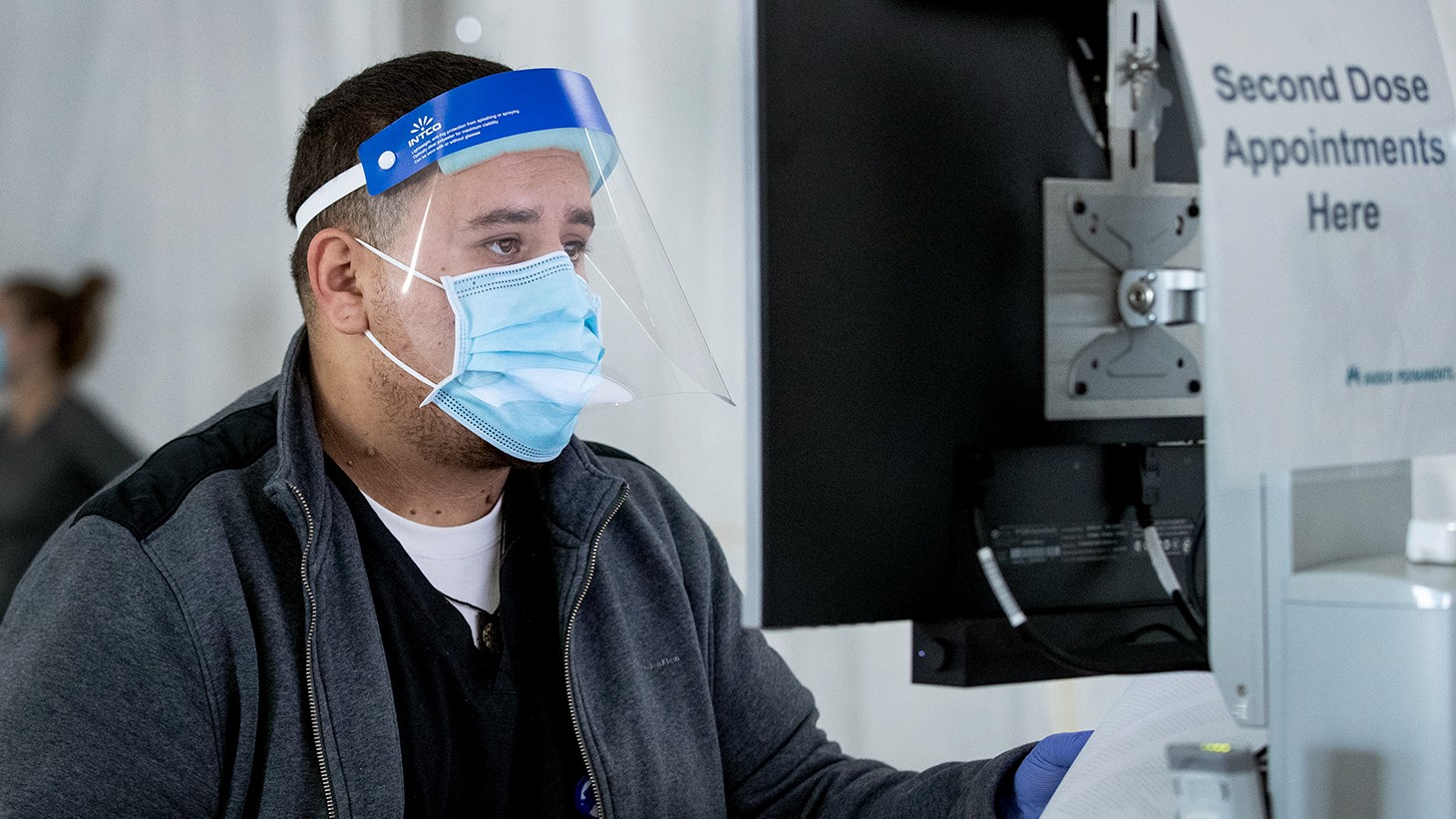 young man wearing a mask, sitting in front of a computer.