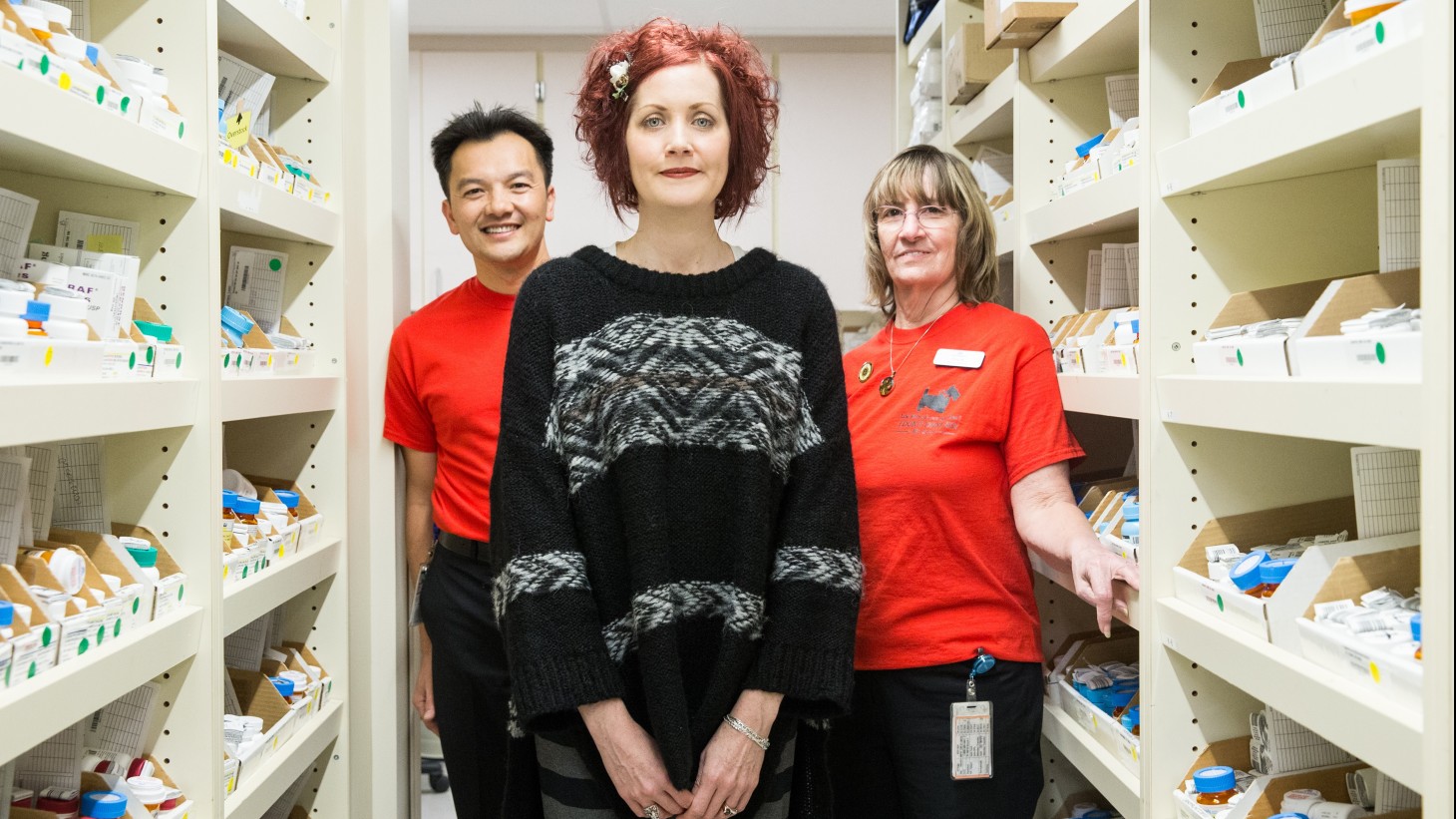 Three people standing amid shelves of pharmacy supplies