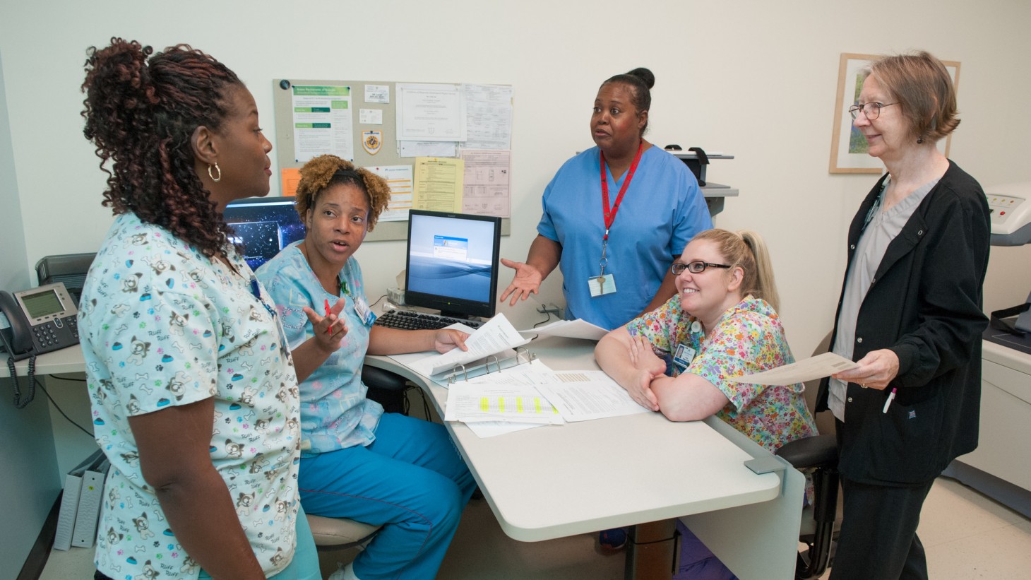 A group of health care workers standing around a desk, talking with each other 