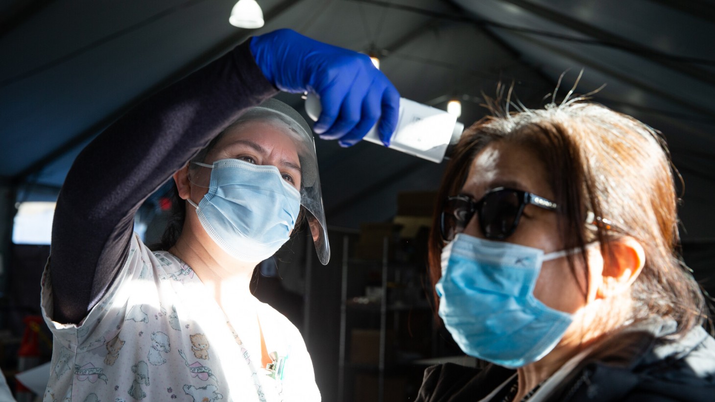 Health care worker wearing face shield takes a patient's temperature