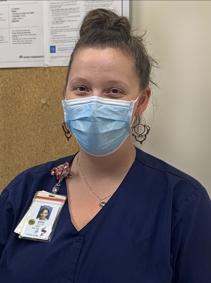 A female health care worker, wearing dark blue scrubs and a light blue mask